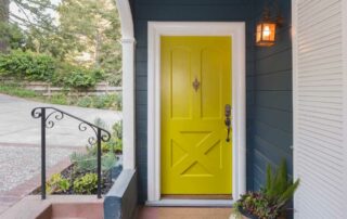 Bright yellow front door on the front of a dark blue painted home