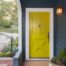 Bright yellow front door on the front of a dark blue painted home