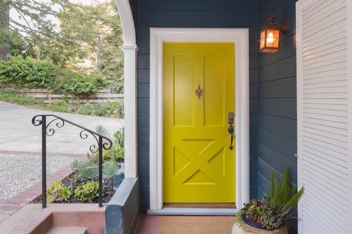 Bright yellow front door on the front of a dark blue painted home