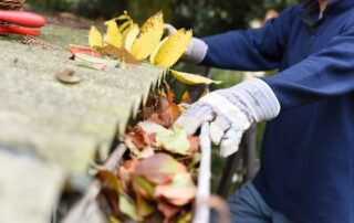 Man wearing work gloves clearing out multicolored leaves from a home gutter