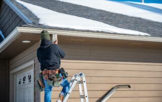 A professional on a ladder wearing a toolbelt and installing new gutters on a residential home at Gilkey Windows & Exterior Solutions near Lexington, KY