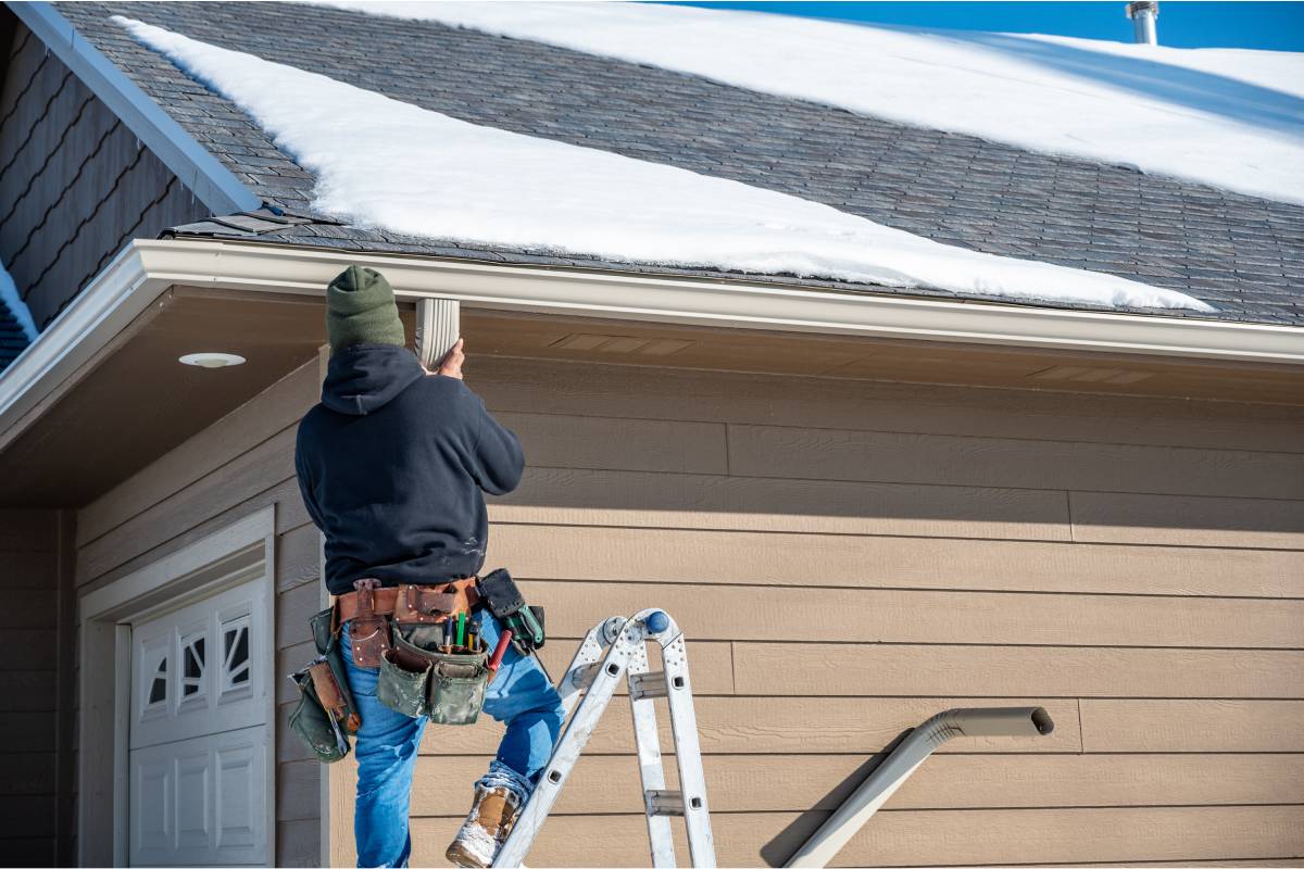 A professional on a ladder wearing a toolbelt and installing new gutters on a residential home at Gilkey Windows & Exterior Solutions near Lexington, KY