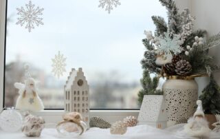 A decorative windowsill with white and neutral-themed holiday decorations featuring pine cones and winter greenery at Gilkey Windows & Exterior Solutions near Lexington, KY