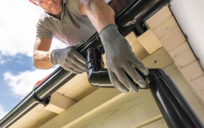 A professional wearing protective gloves while installing chic black gutters on a residential home's exterior at Gilkey Windows & Exterior Solutions near Lexington, KY