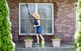 A woman wearing a sunhat using the garden hose to clean her exterior windows at Gilkey Windows & Exterior Solutions near Lexington, KY