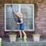 A woman wearing a sunhat using the garden hose to clean her exterior windows at Gilkey Windows & Exterior Solutions near Lexington, KY
