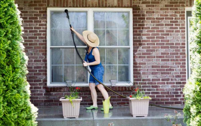 A woman wearing a sunhat using the garden hose to clean her exterior windows at Gilkey Windows & Exterior Solutions near Lexington, KY