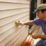 A homeowner wearing a hat and gloves while cleaning his siding using a bristled brush at Gilkey Windows & Exterior Solutions near Lexington, KY