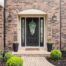 Black front door with glass panels and sidelights on a home's brick exterior and well-manicured yard