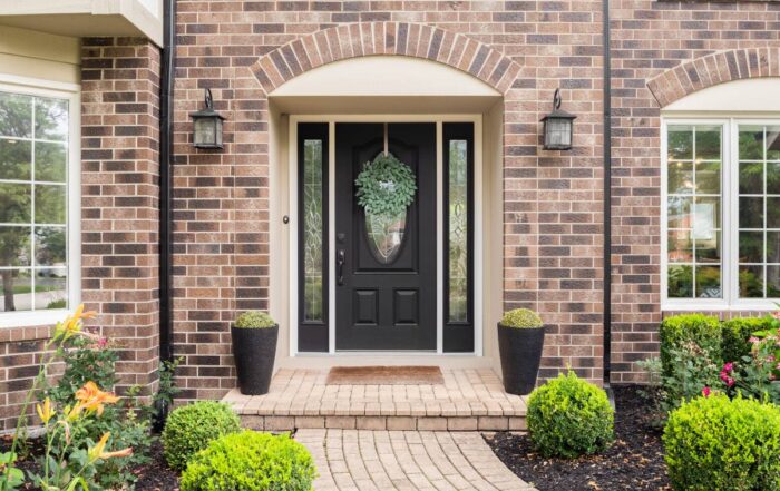 Black front door with glass panels and sidelights on a home's brick exterior and well-manicured yard