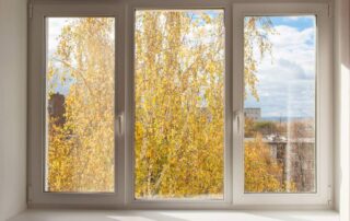 An image of a casement window with white framing, overlooking Autumn yellow trees outside