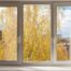 An image of a casement window with white framing, overlooking Autumn yellow trees outside