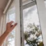Image of someone using their arm to open a window with a white vinyl window frame