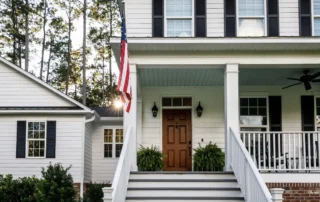A new front door of a home with white siding, changing trees, and an American flag
